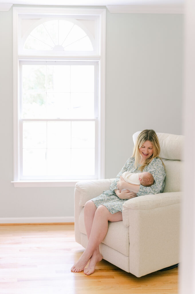 Mom holding newborn baby in rocker in nursery during in-home newborn photography session in Roswell, GA